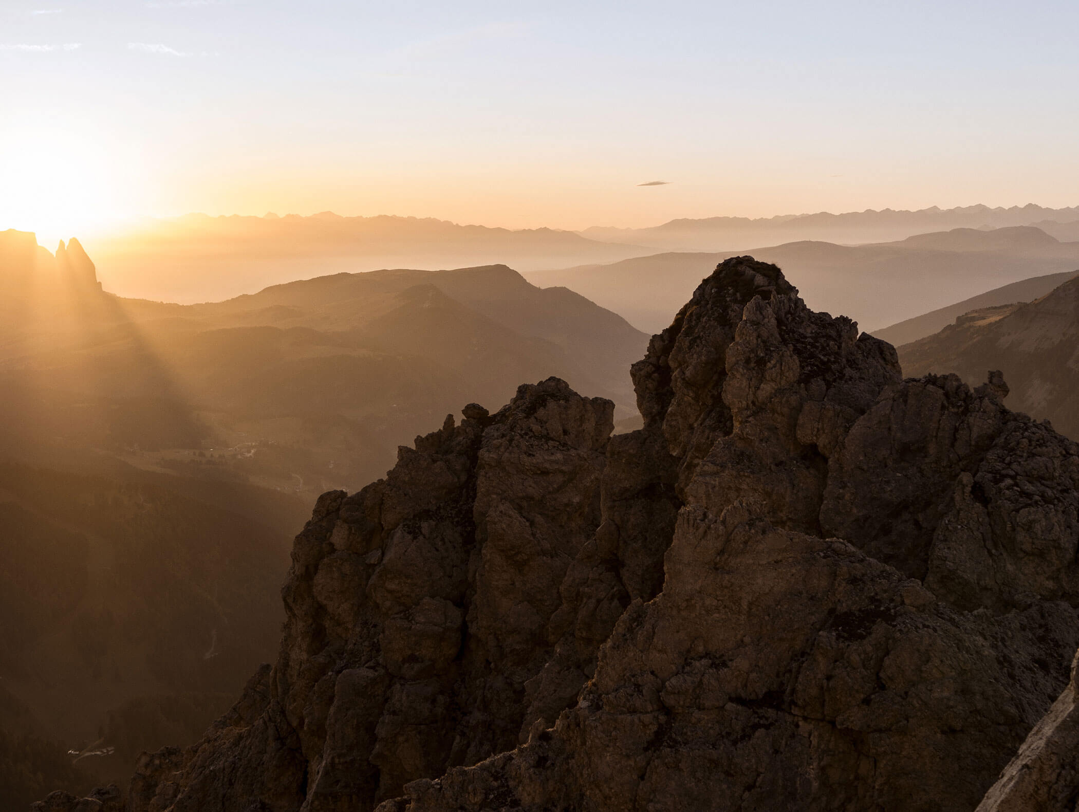 Felsige Berggipfel bei Sonnenaufgang mit Sonnenstrahlen und nebelverhangenen Hügeln im Hintergrund. - Hotel Kristiania