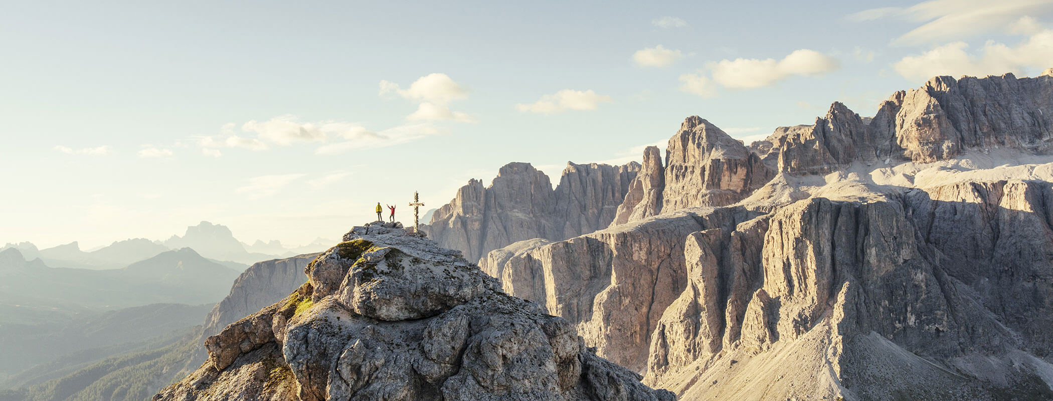 Drei Wanderer stehen auf einem felsigen Berggipfel, im Hintergrund sind unter dem klaren Himmel dramatische Klippen und Berge zu sehen. - Hotel Kristiania