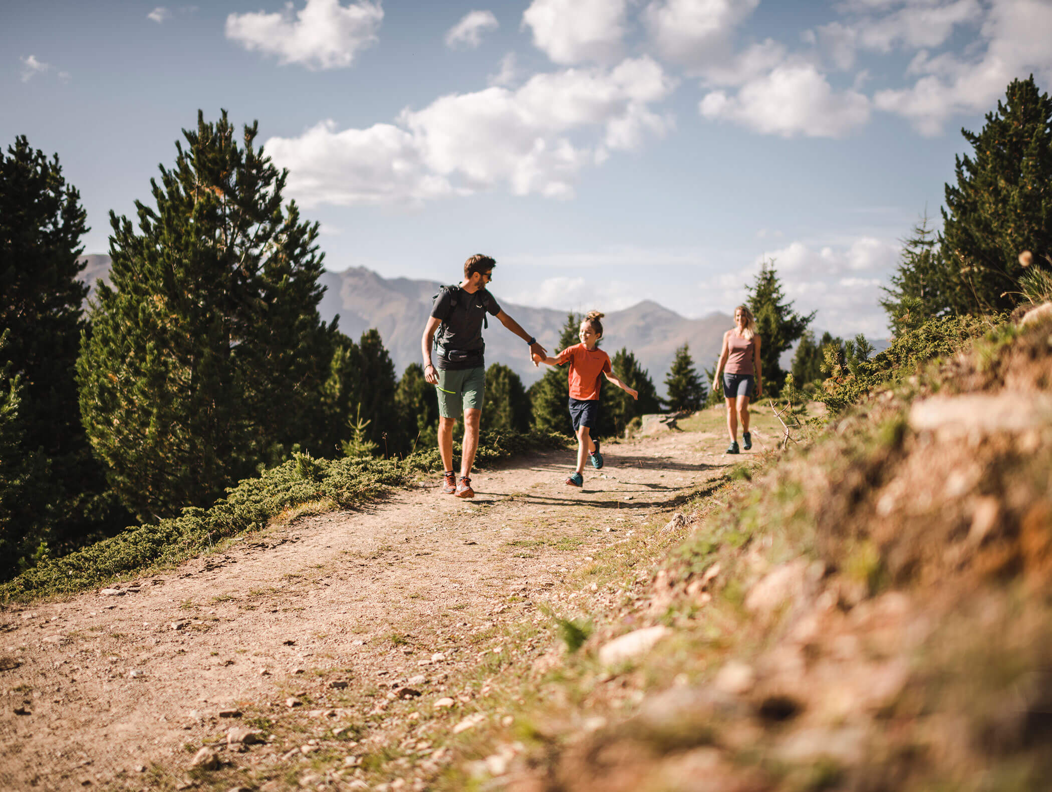 Familienwanderung auf einem sonnigen Bergweg, mit Bäumen und Bergen im Hintergrund. - Hotel Kristiania