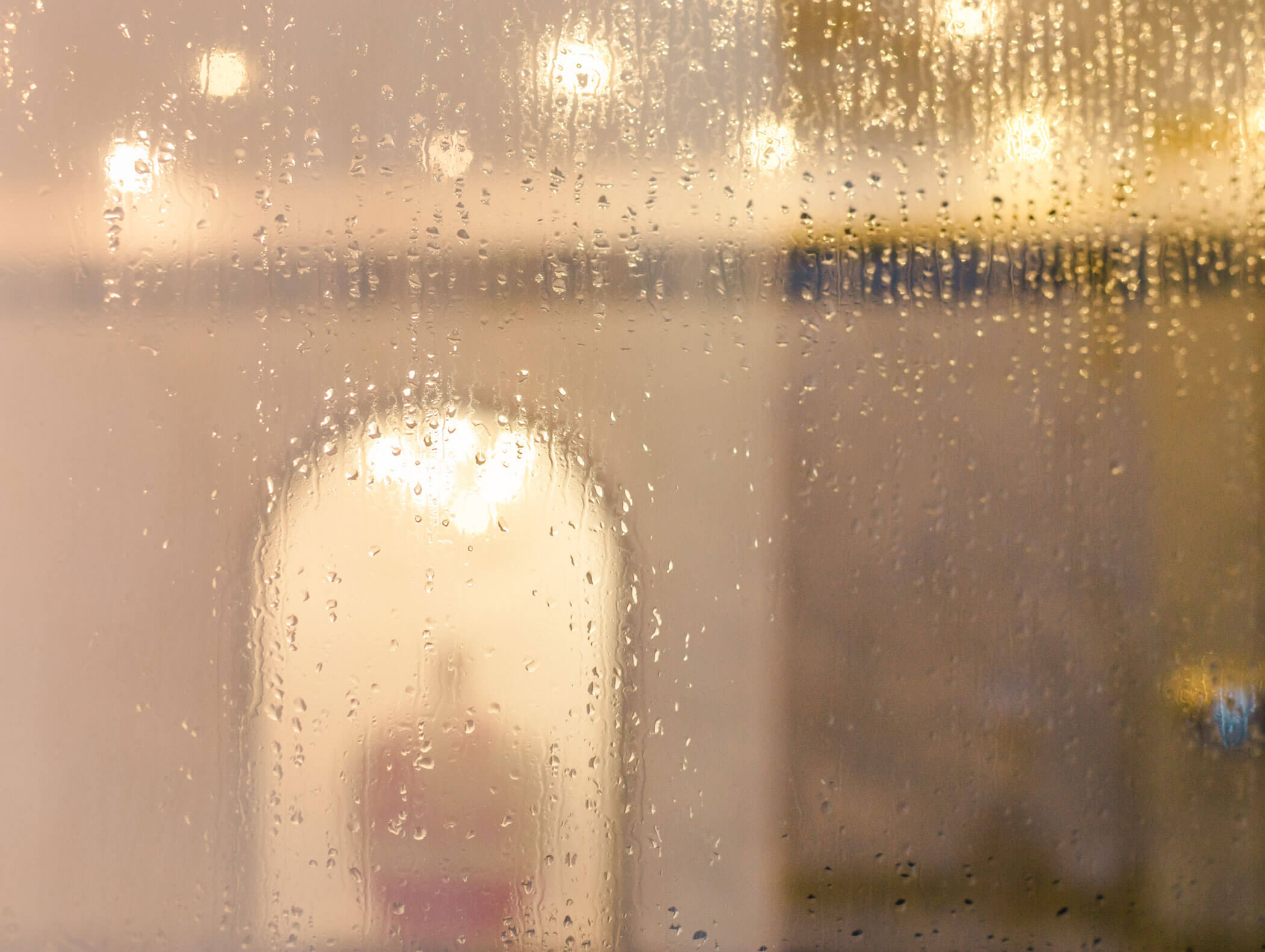 Regentropfen an einem Fenster, dahinter sind verschwommene Lichter im Innenraum und eine gewölbte Tür zu sehen. - Hotel Kristiania