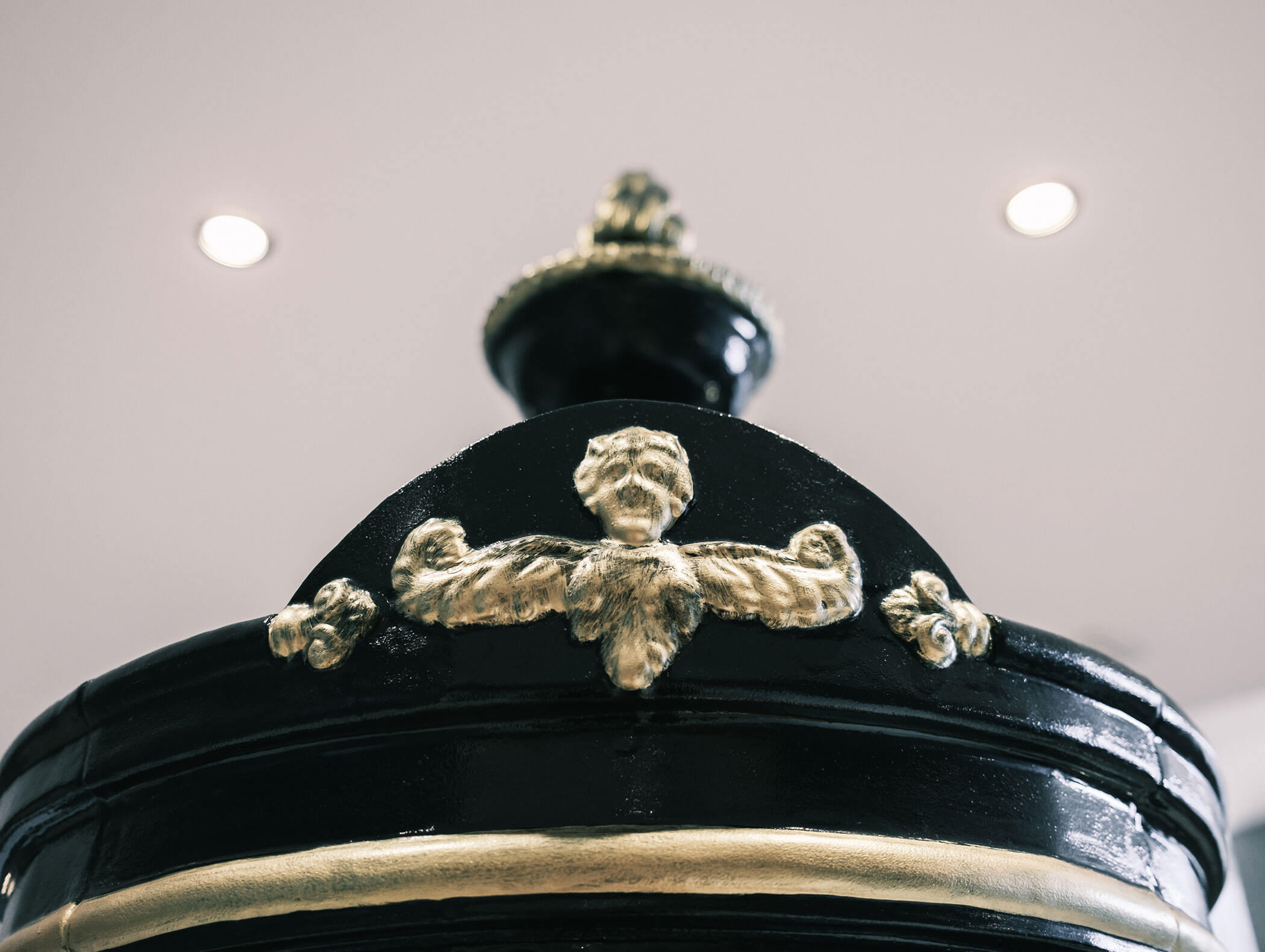 Nahaufnahme eines kunstvoll verzierten schwarzen und goldenen Dekorationsgegenstands mit einem geschnitzten Gesicht und Schnörkelverzierungen. - Hotel Kristiania