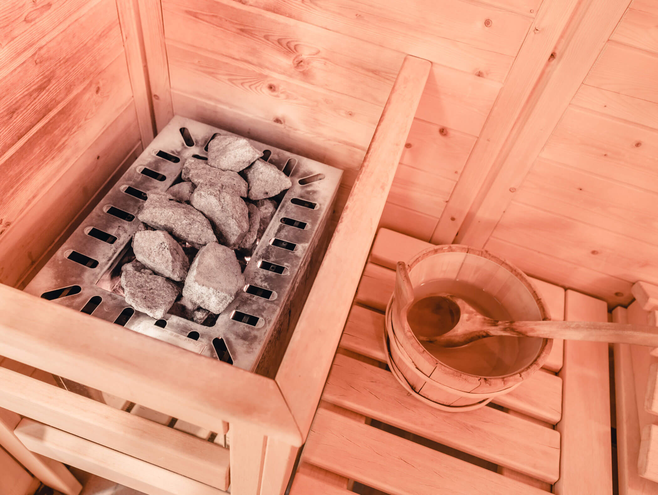 Ein Ofen mit Saunasteinen und einem Holzeimer mit einer Schöpfkelle in einer Saunakabine aus Holz. - Hotel Kristiania