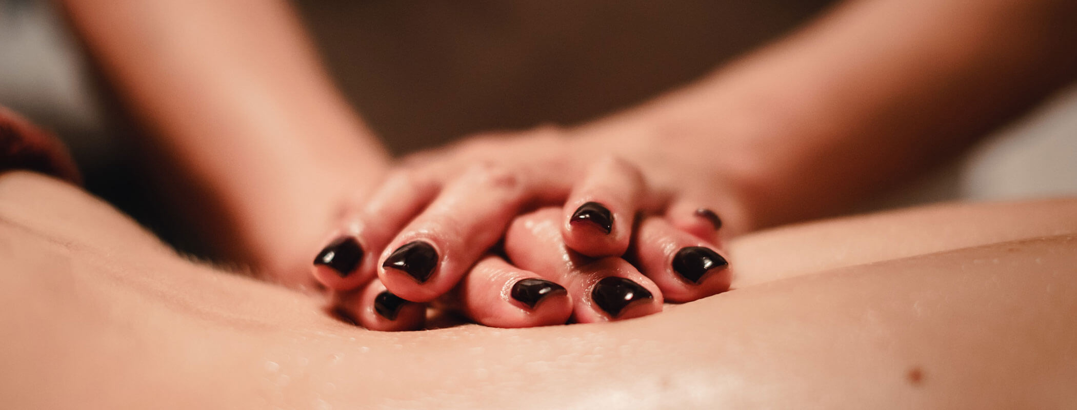 Nahaufnahme von Händen mit dunklem Nagellack, die eine Rückenmassage auf nackter Haut durchführen. - Hotel Kristiania