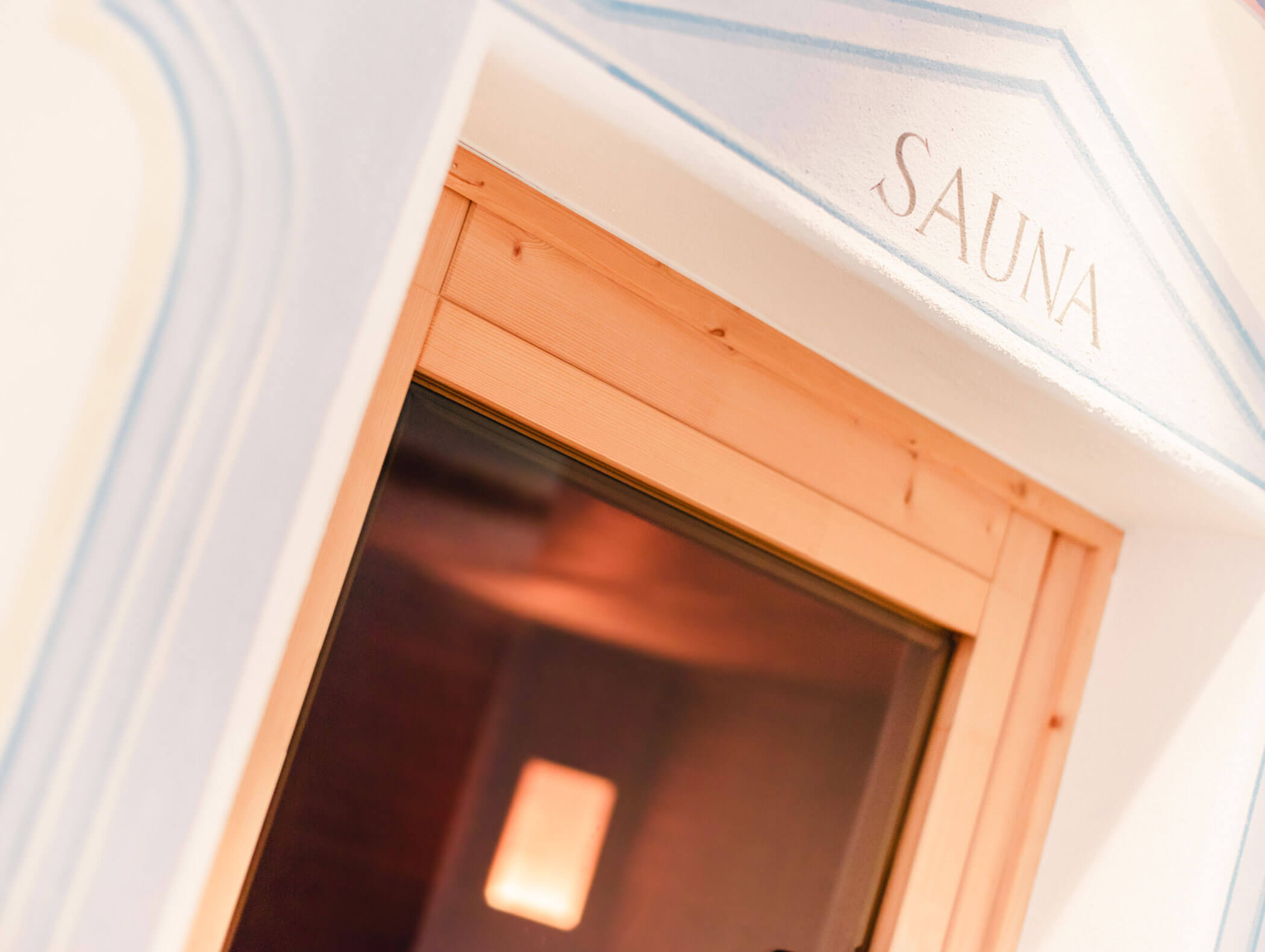 Nahaufnahme einer Saunatür aus Holz mit einem Fenster, über dem Eingang steht die Aufschrift „SAUNA“. - Hotel Kristiania