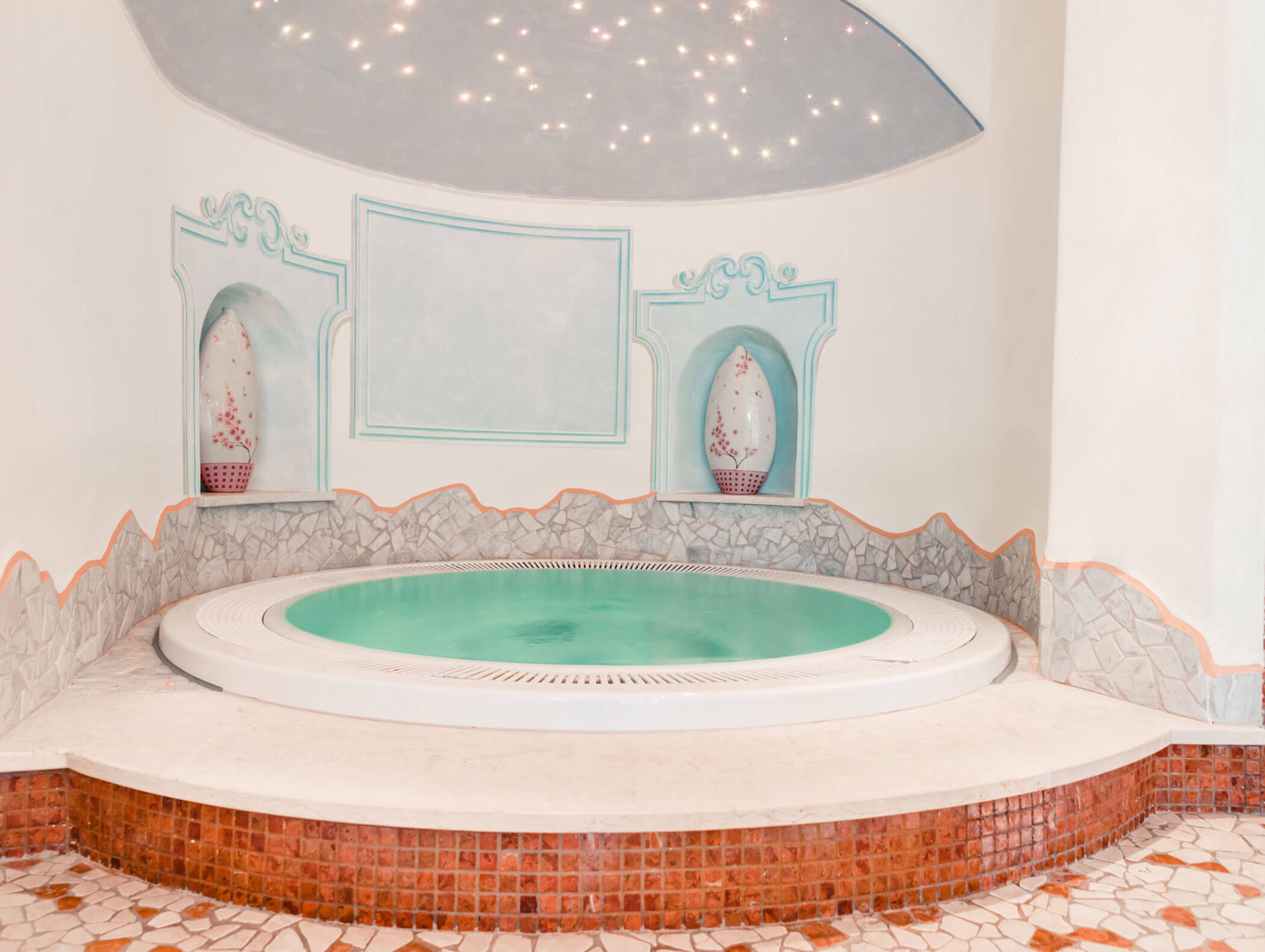 Ein Whirlpool im Innenbereich mit türkisfarbenem Wasser, Steinfliesen und dekorativen Vasen in Nischen unter einer Sternendecke. - Hotel Kristiania