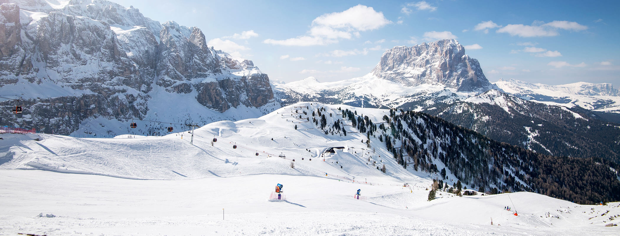 Paesaggio montano innevato con sciatori sulle piste, cime rocciose e cielo azzurro con nuvole sparse. - Hotel Kristiania
