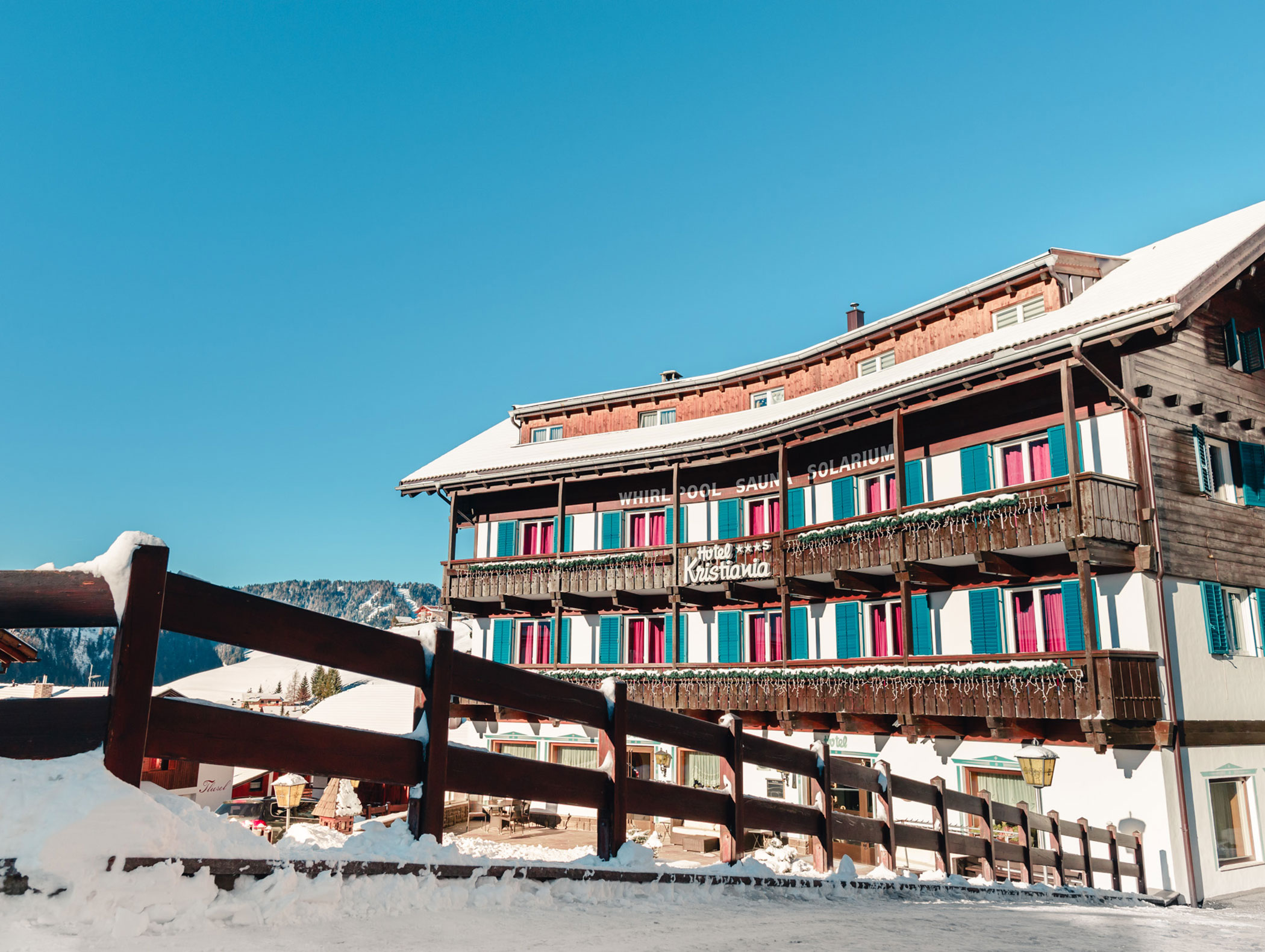 Un hotel alpino in legno con persiane colorate e i dintorni innevati sotto un cielo limpido e azzurro. - Hotel Kristiania