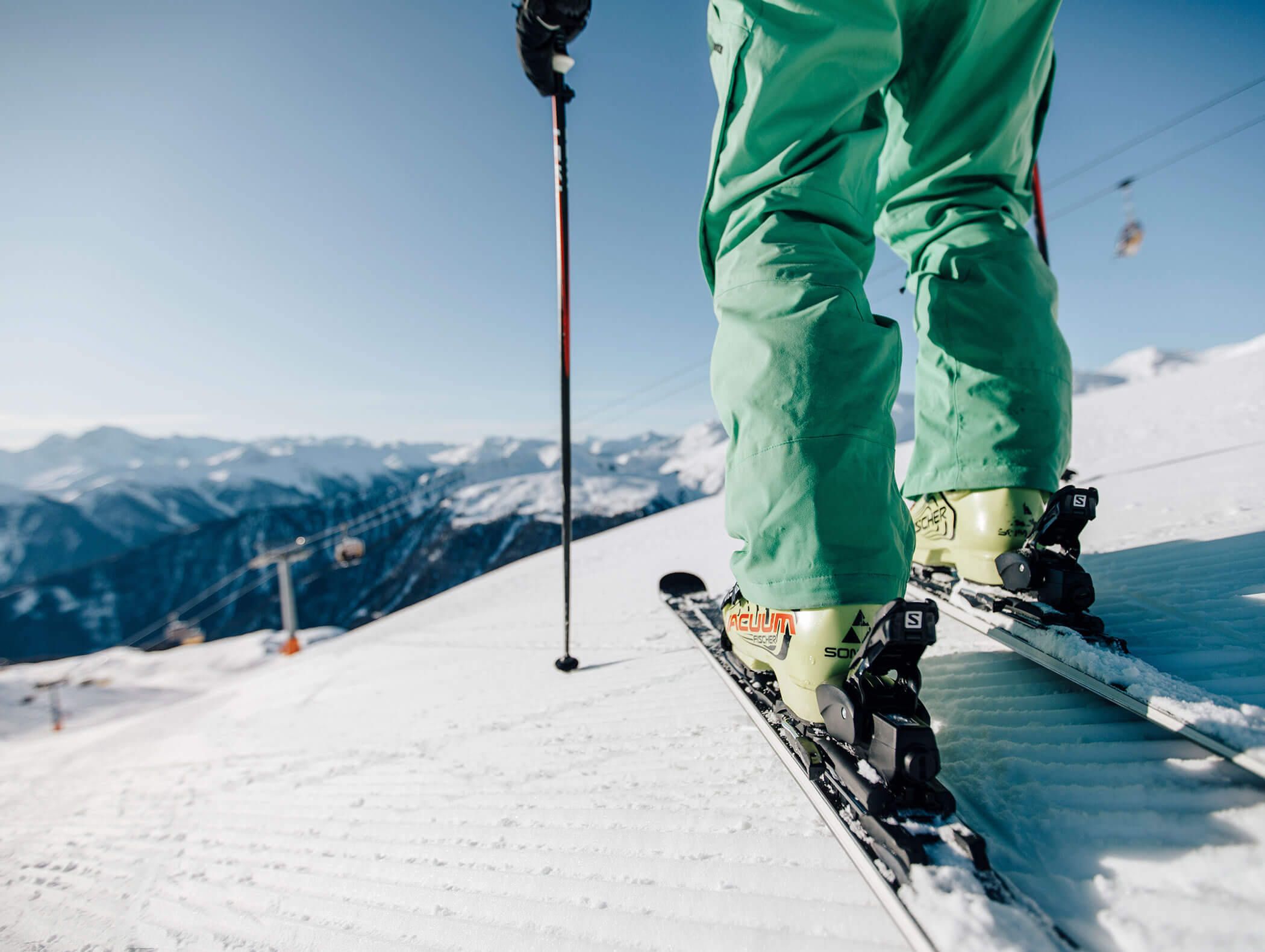 Primo piano di uno sciatore con pantaloni verdi in piedi su un pendio innevato, con le montagne sullo sfondo. - Hotel Kristiania