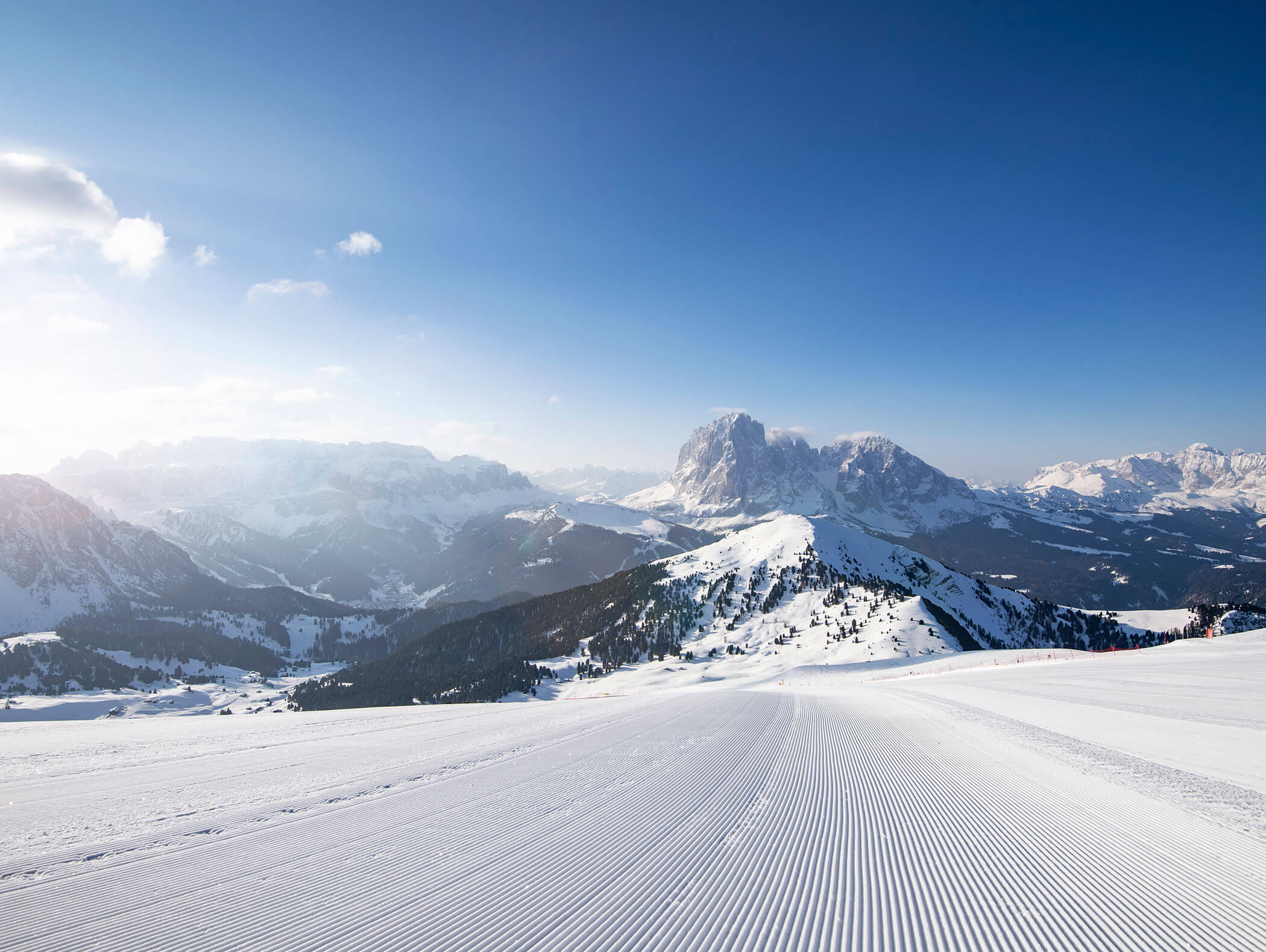 Pista da sci ben battuta che conduce verso montagne innevate sotto un cielo azzurro e limpido, con vette in lontananza e raggi di sole. - Hotel Kristiania