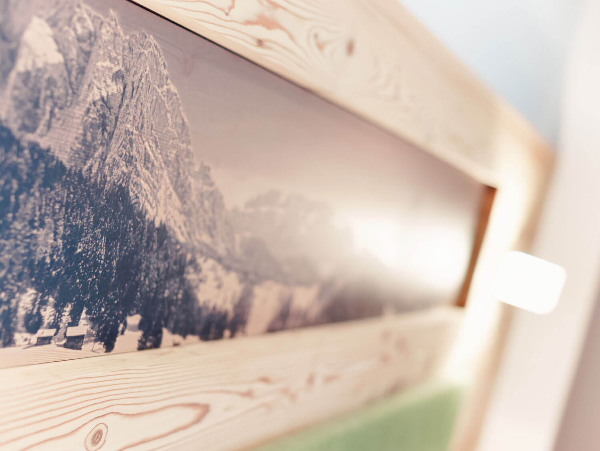 Foto sfocata incorniciata di un paesaggio montano appesa a una parete di legno chiaro, con una luce soffusa proveniente da destra. - Hotel Kristiania