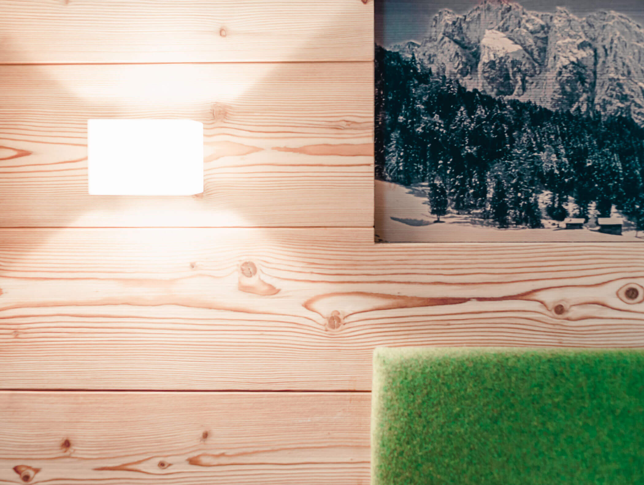 Una lampada da parete accesa su un rivestimento in legno chiaro, con un cuscino verde e una foto di una montagna innevata appesa alla parete. - Hotel Kristiania