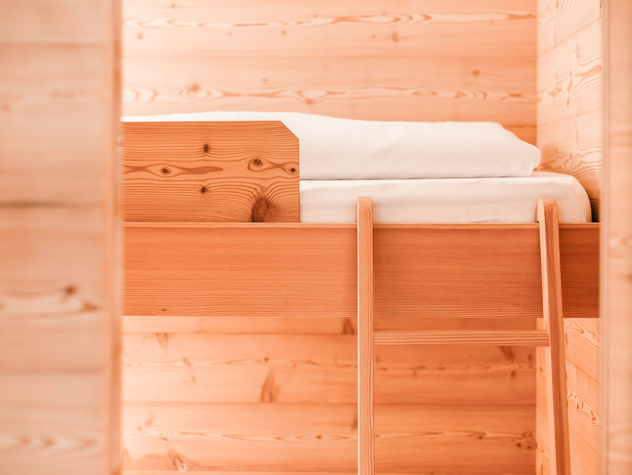 Letto a castello superiore con lenzuola bianche piegate in una stanza con arredi in legno, con una scaletta in legno che porta al letto. - Hotel Kristiania