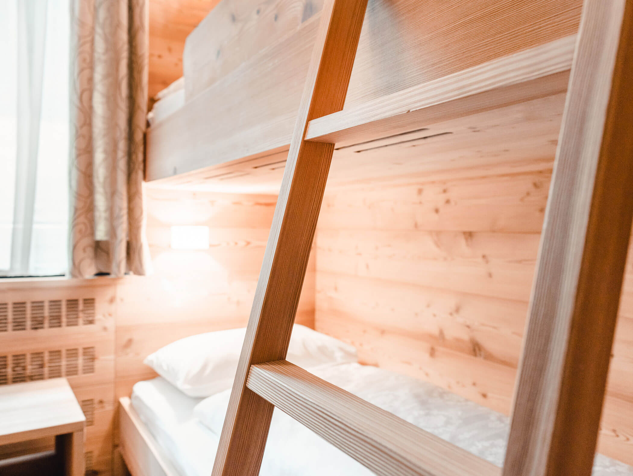 Letto a castello in legno con biancheria da letto bianca e una scaletta, in una stanza luminosa e accogliente con pareti rivestite in legno. - Hotel Kristiania