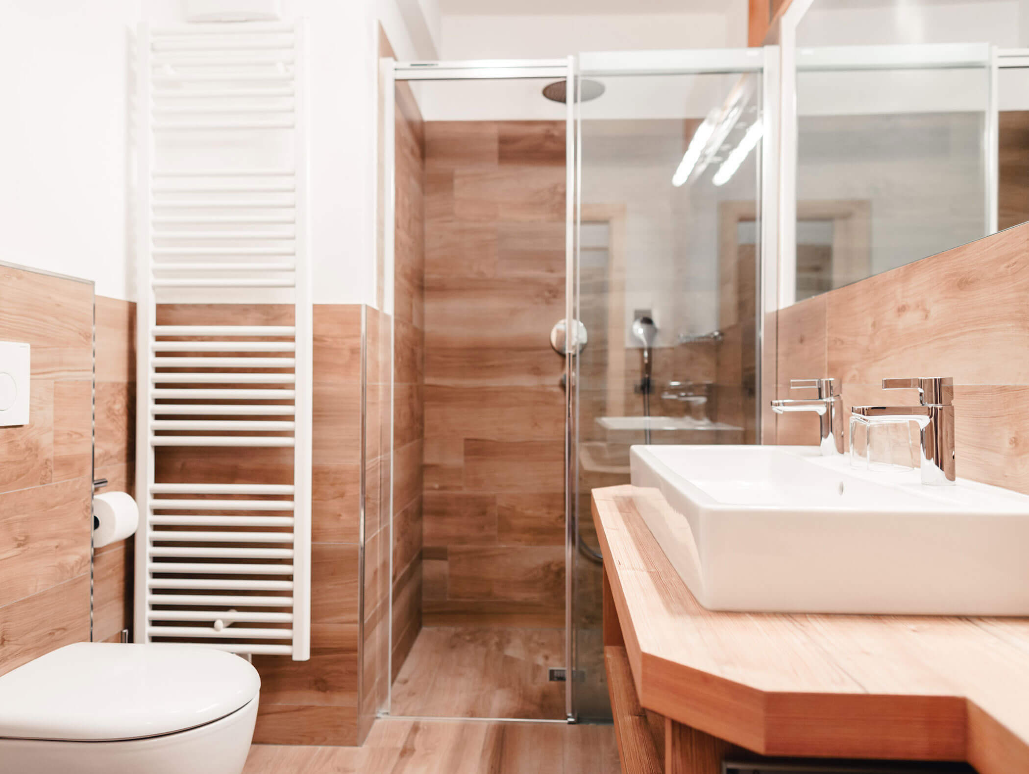 Bagno moderno con dettagli in legno, box doccia in vetro, lavabo bianco, WC e scalda asciugamani. - Hotel Kristiania