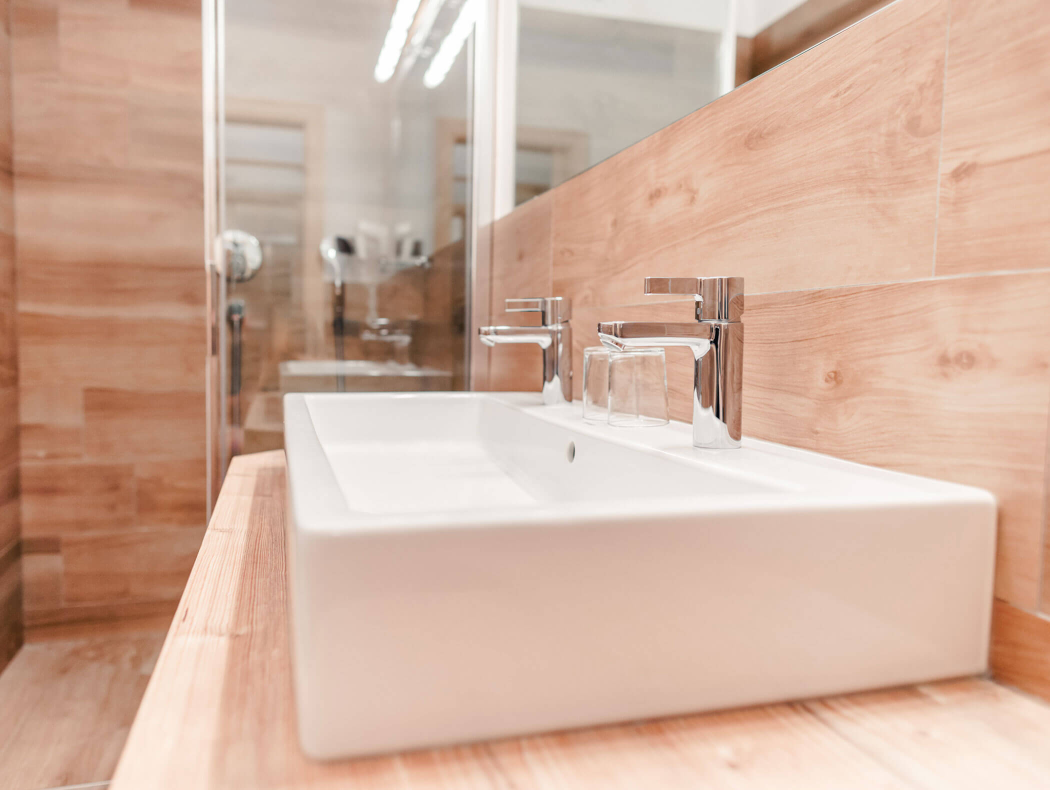 Bagno moderno con lavabo rettangolare bianco, rubinetteria cromata e pareti e piano di lavoro effetto legno. - Hotel Kristiania