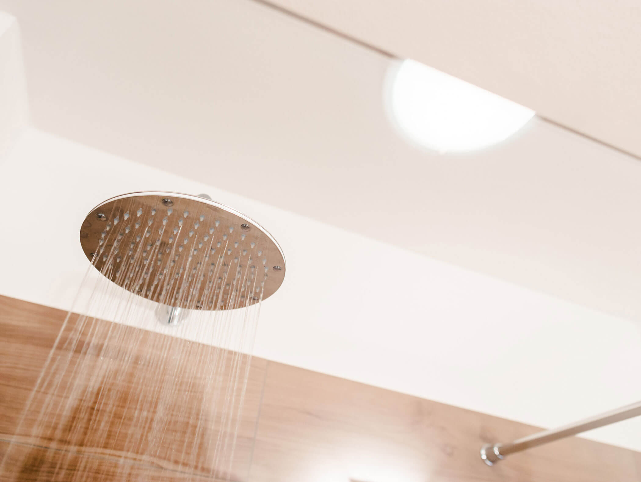 Un moderno soffione della doccia da cui scorre l'acqua, montato su una parete rivestita con piastrelle effetto legno. - Hotel Kristiania