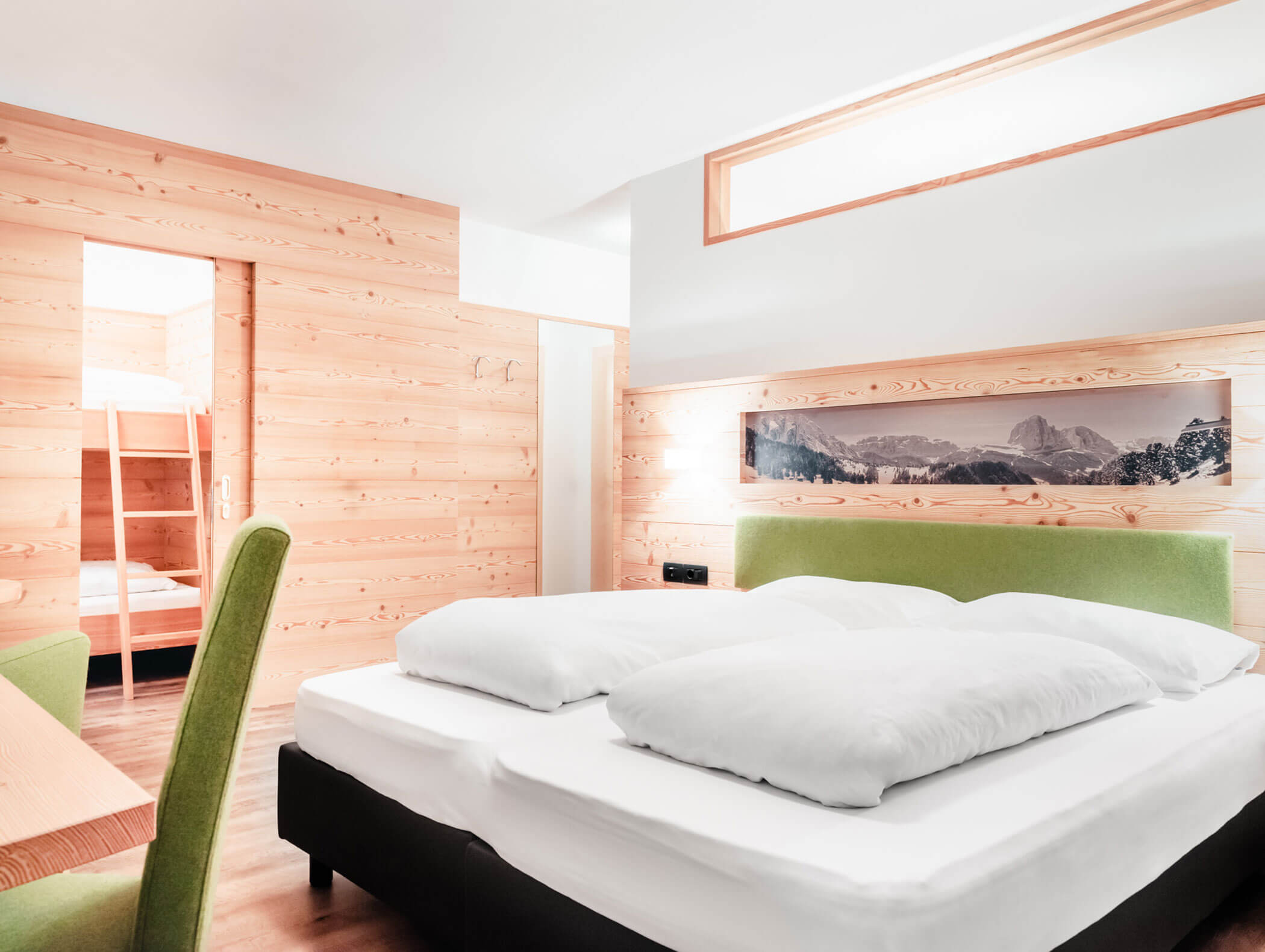 Camera d'albergo luminosa e moderna con un letto verde, pareti in legno e, sullo sfondo, una porta che conduce alla zona con i letti a castello. - Hotel Kristiania